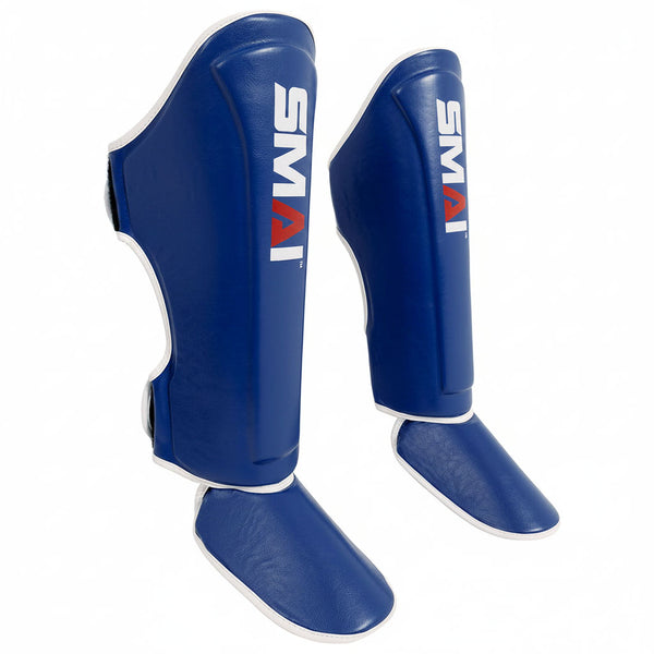 The Essentials Muay Thai Shin Instep Guard - Blue by SMAI features white trim and the "SMAI" logo in white and red on the front. Made from durable synthetic leather, it offers reliable shin and instep protection. Displayed on a white background.