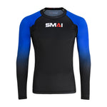 The SMAI Long Sleeve Rash Guard - Blue features a black body, blue gradient sleeves, and white/red "SMAI" chest branding. Designed for no-gi grappling with advanced compression technology. Shown on a plain white background.