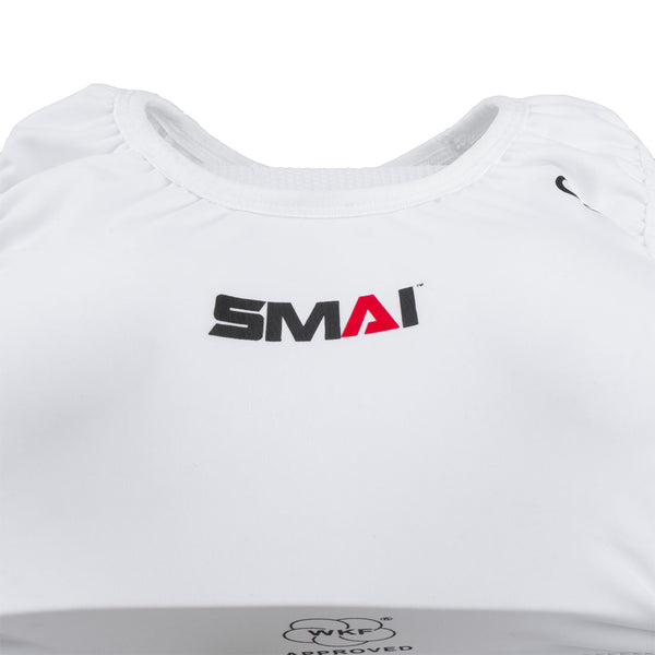 A close-up of the SMAI WKF Approved Female Body Guard with Breast Plate shows a white breast plate featuring the "SMAI" logo in black and red, shoulder pads, a smooth texture, and a circular approval logo at the bottom.