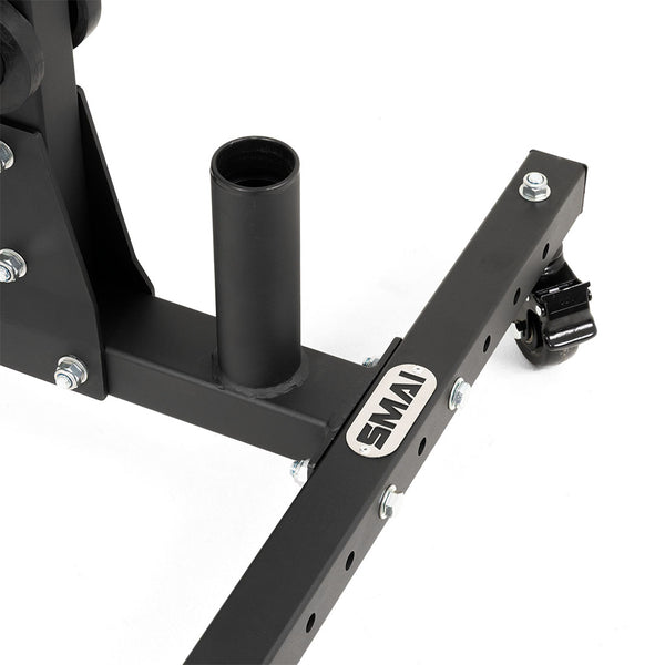 Close-up of the SMAI Bumper Plate & Barbell Storage Tree with Wheels, showing its black metal base, vertical cylindrical barbell holder, crossbar with bolted joints, branded "SMAI" plate, and caster wheel on a white background.