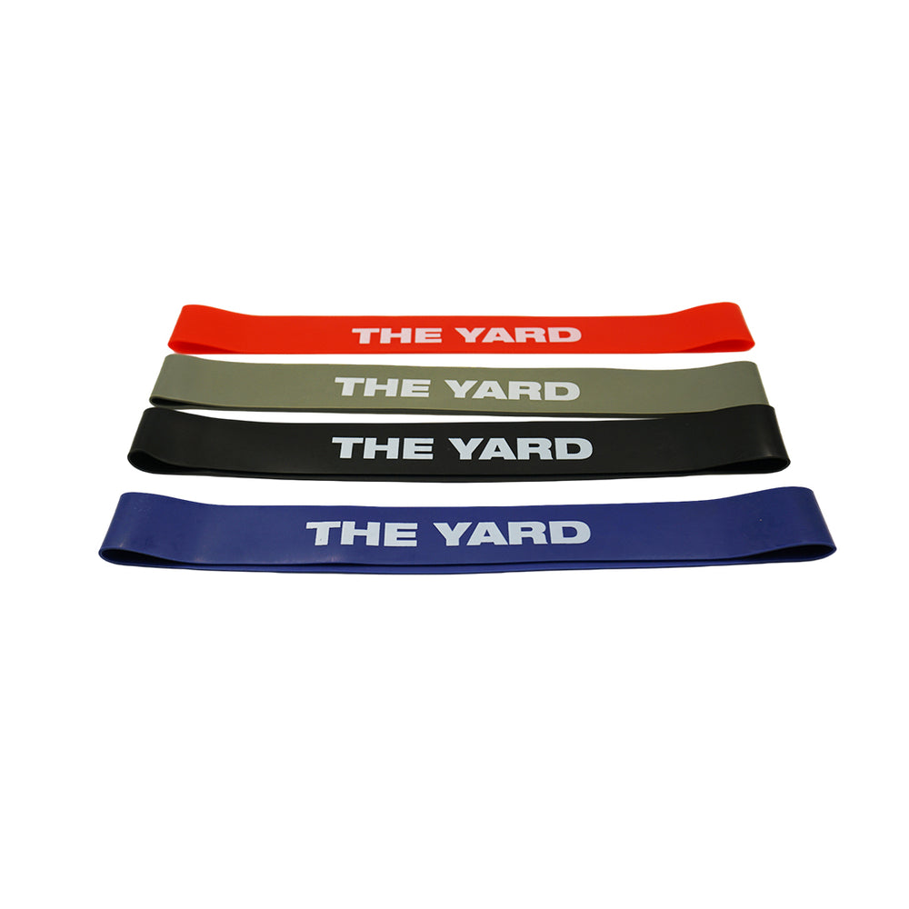 The SMAI The Yard - Rubber Mini Resistance Bands Set of 4 features red, gray, black, and blue bands printed with "THE YARD" in white, arranged flat on a white background—ideal for your next booty workout.