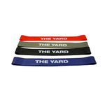 The SMAI The Yard - Rubber Mini Resistance Bands Set of 4 features red, gray, black, and blue bands printed with "THE YARD" in white, arranged flat on a white background—ideal for your next booty workout.