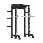 The SMAI Half Power Rack with Smith Machine from the Vanta Series features a durable black frame with numerous holes for adjustable height settings and handy side pegs for organizing weights, highlighting its adaptable design. A barbell is securely positioned on the safety pins inside the rack, embodying the strength of the Vanta Series.