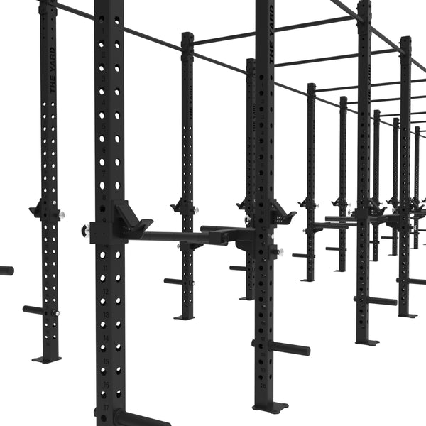 A row of SMAI’s The Yard - Rig - 10 Squat Cell features black steel squat racks with adjustable supports, pull-up bars, and plate holders—offering a robust, modular freestanding gym solution for commercial setups.