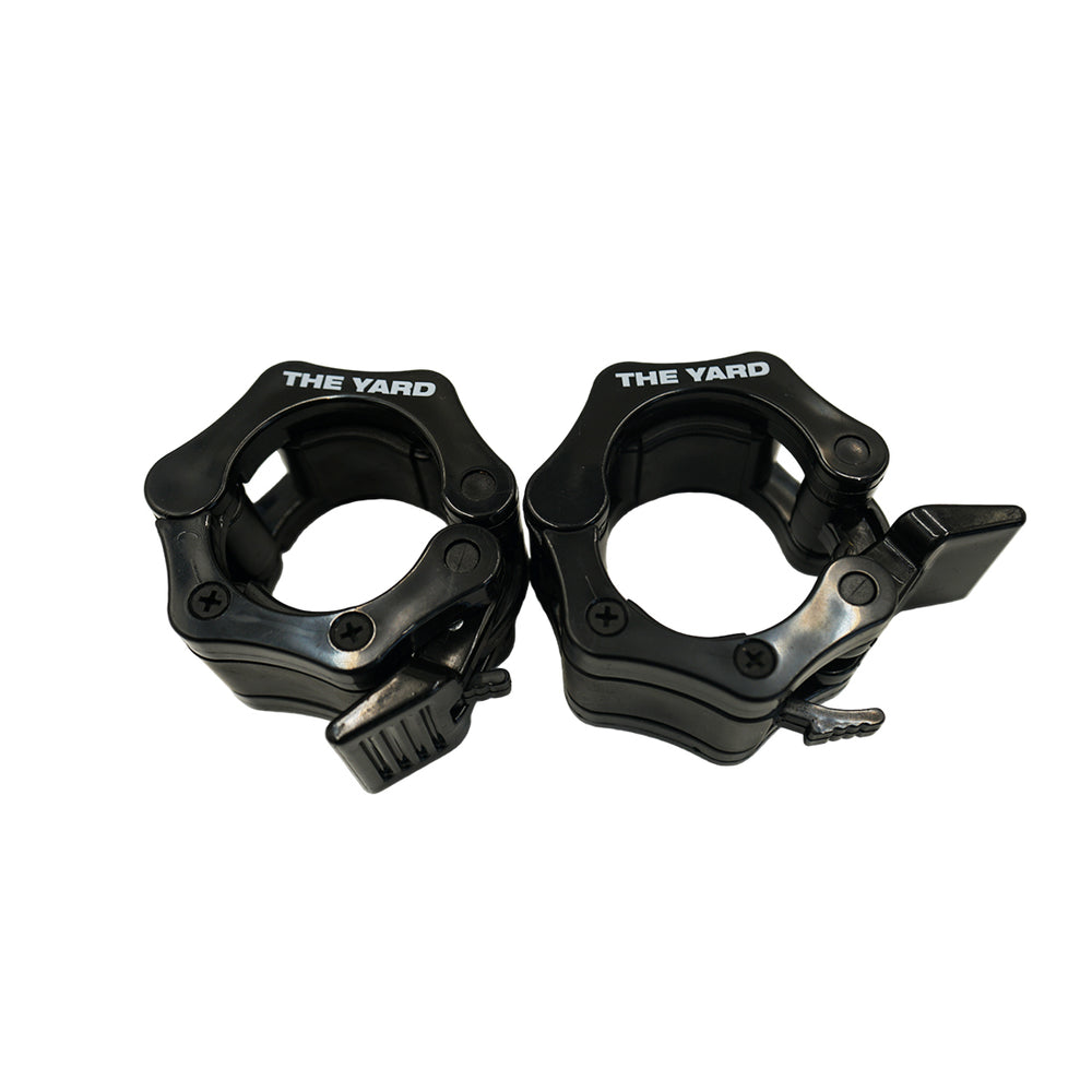 A pair of SMAI The Yard - Barbell - Easy Lock 50mm Collars (black) feature locking levers to securely hold weight plates. These durable collars are shown side by side on a white background.