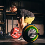 A man in a black shirt and yellow shorts prepares to deadlift a barbell loaded with SMAI Calibrated Weight Plates - 10kg (Pair) in a gym.
