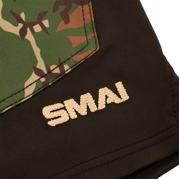 Close-up of SMAI Shorts - Cross Training Camo, featuring a green and brown camouflage pattern, black panel with beige "SMAI" embroidery, and durable gusset construction for enhanced flexibility.
