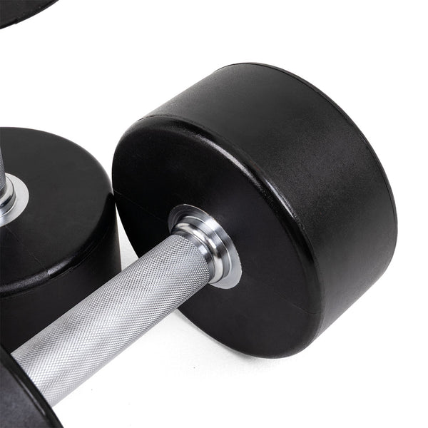 Close-up of SMAI Commercial Round Dumbbells (Pair) in black with a textured silver handle on a white surface. Another similar SMAI dumbbell is partially visible in the background, ideal for any home gym setup.