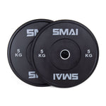 A pair of SMAI Home Gym Bumper Plates - 5kg, featuring sleek black design and clear SMAI branding, are stacked with one slightly overlapping the other against a white background—ideal for any home gym setup.