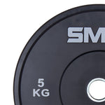 A close-up of a black SMAI Home Gym Bumper Plate 5kg with "5 KG" in white and part of the SMAI logo at the top. This Olympic bumper plate features a metal center ring.