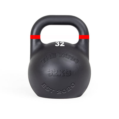 The SMAI The Yard - Competition Steel Kettlebell 32kg is black with a red stripe near the handle, features "THE YARD 32KG EST 2020" embossed on the front and "32" in white below the handle, and has a consistent size design.