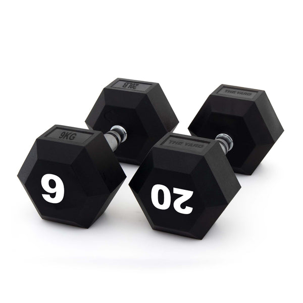 Three black SMAI The Yard - Rubber Hex Dumbbells with metal handles are arranged on a white background. Two commercial gym dumbbells display "9 KG" and "20 KG" in large white numbers on their ends.