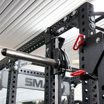 Close-up of a Smith Machine Insert from the Vanta Series by SMAI, featuring adjustable safety bars and weight pegs. Constructed from black metal, it includes numbered holes for height adjustments, set in an indoor gym designed for weightlifting enthusiasts.