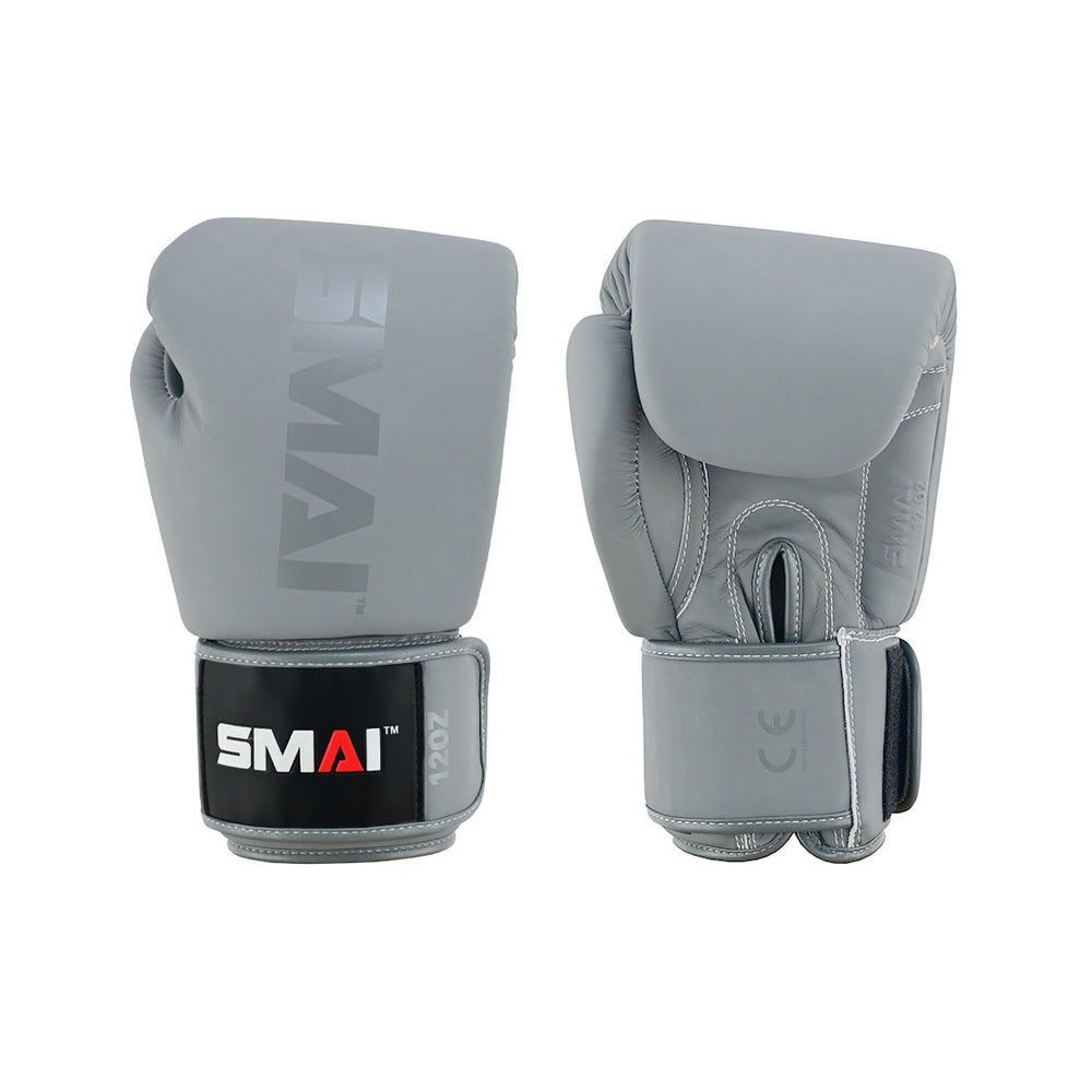 The SMAI Elite85 Boxing Glove in Charcoal features quality cowhide leather, black wrist straps, "SMAI" branding, and a "12oz" weight mark. One glove is palm down and one is palm up, showcasing the craftsmanship and branded details.