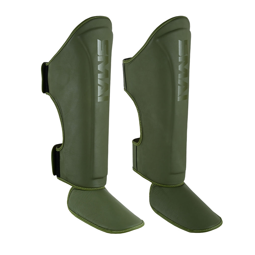 The SMAI PRE ORDER: Elite85 Muay Thai Shin Guards in olive green feature foot protection and velcro straps, designed for martial arts or sports, displayed against a white background.