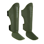 The SMAI PRE ORDER: Elite85 Muay Thai Shin Guards in olive green feature foot protection and velcro straps, designed for martial arts or sports, displayed against a white background.