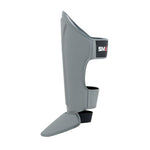 The SMAI Elite85 Muay Thai Shin Guards in charcoal are lightweight with foot protection and a black strap showing "SMAI," ideal for martial arts or Muay Thai training.
