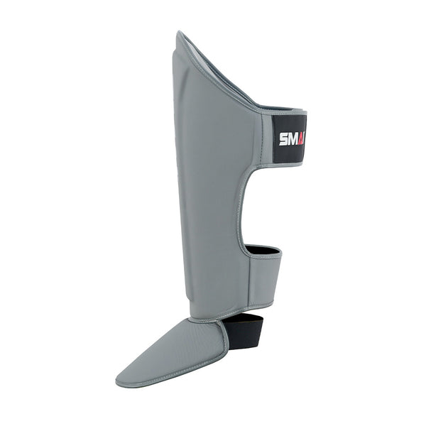 The SMAI Elite85 Muay Thai Shin Guards in charcoal are lightweight with foot protection and a black strap showing "SMAI," ideal for martial arts or Muay Thai training.