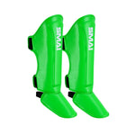 Vivid green Essentials Muay Thai Shin Guards for kids by SMAI are shown against a white background, featuring the brand’s white logo, black adjustable straps around the calf and ankle, and designed as part of the Clearance Line.