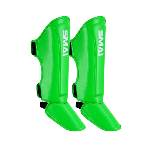 Vivid green Essentials Muay Thai Shin Guards for kids by SMAI are shown against a white background, featuring the brand’s white logo, black adjustable straps around the calf and ankle, and designed as part of the Clearance Line.