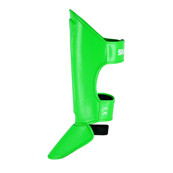 The SMAI Essentials Muay Thai Shin Guards Kids - Green feature an attached foot protector and adjustable straps for martial arts protection, shown on a white background.