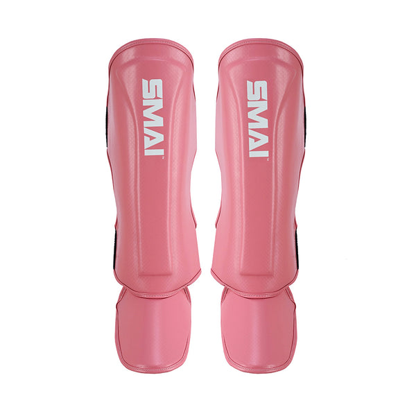 The SMAI Essentials Muay Thai Shin Guards Kids - Pink offer durable shin protection for children, featuring the brand name in white on each guard. Displayed side by side on a white background, they're ideal as kids' protective gear.