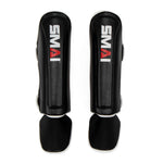 A pair of black Essentials Muay Thai Shin Guards for kids by SMAI, each featuring a white and red “SMAI” logo, with attached foot protectors—shown on a white background and designed to provide ideal martial arts protection for children.