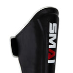 A close-up of a black Essentials Muay Thai Shin Guard - Kids by SMAI, featuring white trim and the brand name “SMAI” printed in bold white and red lettering on the front, designed for versatile protection as both shin instep guards and kids shin guards.