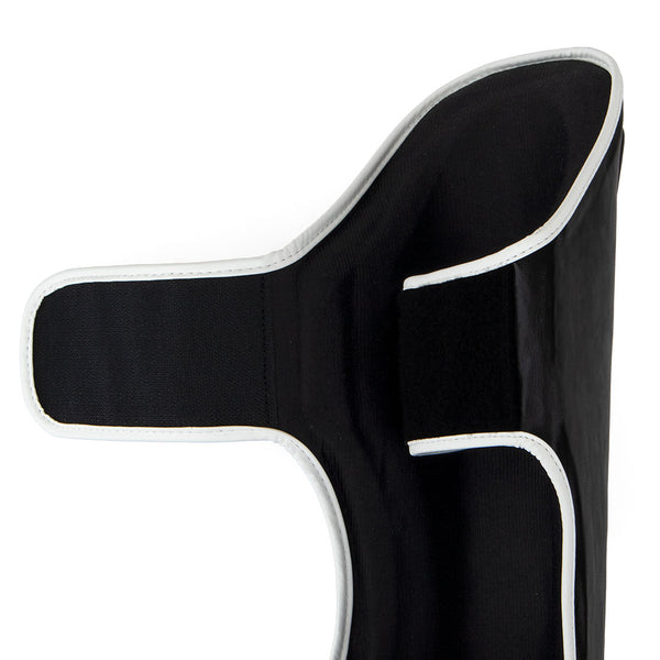 The SMAI Essentials Muay Thai Shin Guards - Kids are black orthopedic shin guards with white trim, displayed open with Velcro straps extended against a white background—ideal for providing added support and protection as children’s shin or shin instep guards during martial arts activities.