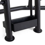 Close-up of the SMAI Pump Set - Storage Rack, a black metal unit with a rectangular box or tray placed between two vertical poles. This rack is part of a larger apparatus, like furniture or equipment, with visible bolts for assembly.