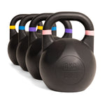 Four SMAI Competition Kettlebell - Fusion Series kettlebells, finished in black with colored bands on their handles, are arranged in a diagonal row. The nearest kettlebell is labeled 8KG / 18LB.