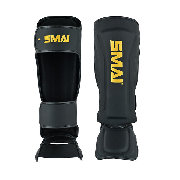Two SMAI PRE ORDER Gold Series Muay Thai Shin Guards in black/gold with yellow branding, multi-layer shock absorption, and high-density foam. Feature straps and padded shin/instep sections. Shown front and back.