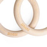The SMAI Wooden Gym Rings with Numbered Straps feature two light wood rings engraved with "SMAI," overlapping on a white background. The set includes adjustable numbered straps and an aluminum clamp for secure installation.