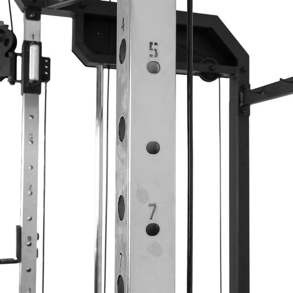Close-up of a metal SMAI All-In-One Home Gym Trainer - Plate Loaded - Demo Stock frame, showing numbered adjustment holes (4, 5, 7). Cables and structural bars from this home gym are visible in the background.