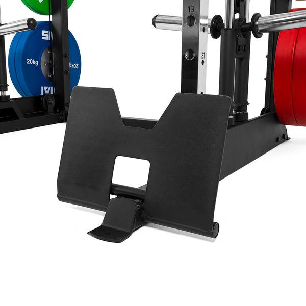 Close-up of a black metal deadlift jack on the floor, positioned in front of the SMAI All-In-One Home Gym Trainer - Plate Loaded (Demo Stock), with colored weight plates mounted in the background.