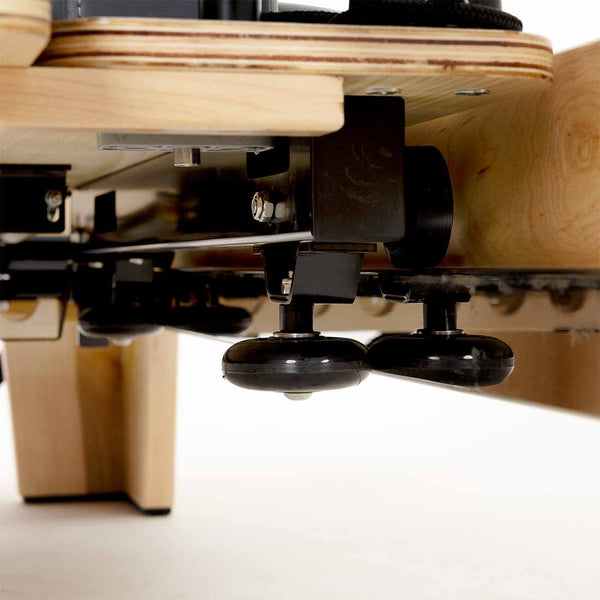 Close-up view of the underside of the SMAI Pilates - Classical Maple Reformer, showing black metal and plastic components against a white background.
