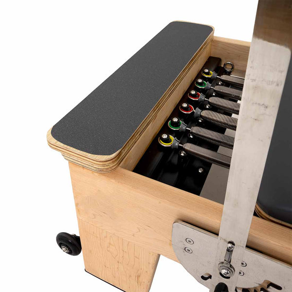 Close-up of the SMAI Pilates - Classical Maple Reformer, showcasing its colored spring resistance system, padded black surface, and adjustable footbar—a premium choice in adjustable Pilates equipment.