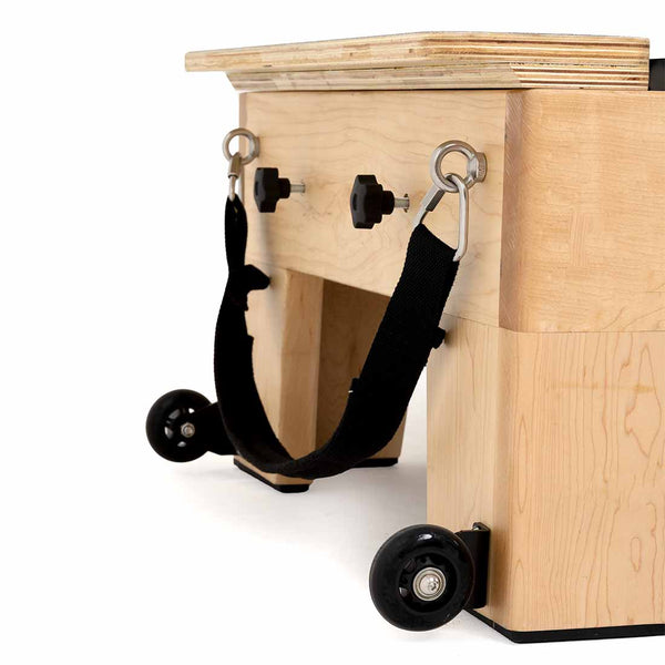 A close-up of the SMAI Pilates - Classical Maple Reformer, showcasing wooden construction, black caster wheels, metal rings, adjustable knobs, and a black side strap.