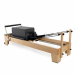 The SMAI Pilates - Classical Maple Reformer is a wooden commercial machine with a padded black platform, foot bar, and adjustable resistance straps, ideal for fitness and exercise workouts.