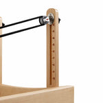 A close-up of the SMAI Pilates - Classical Maple Reformer frame features a vertical scale numbered 1–10 and black resistance cords passing through a top pulley.