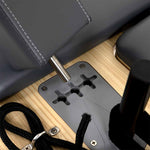 Close-up of a metal rod in a gray mount on a light wood surface, part of the SMAI Pilates - Classical Maple Reformer, with black ropes and padded gray surfaces in view.