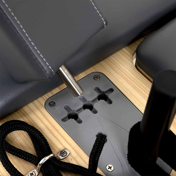 Close-up of a metal rod in a gray mount on a light wood surface, part of the SMAI Pilates - Classical Maple Reformer, with black ropes and padded gray surfaces in view.