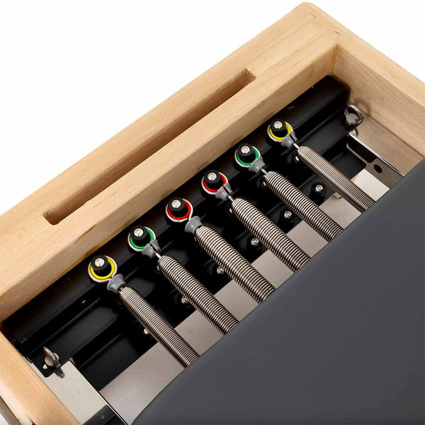 Close-up of the SMAI Pilates - Classical Maple Reformer, featuring five metal resistance springs on color-coded knobs and a black padded surface. This adjustable equipment has a sturdy maple wooden frame for versatile workouts.