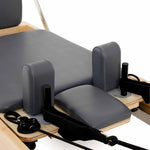 Close-up of the SMAI Pilates - Classical Maple Reformer, featuring padded gray cushions, black straps, and a durable maple wood frame for supportive, effective Pilates workouts.