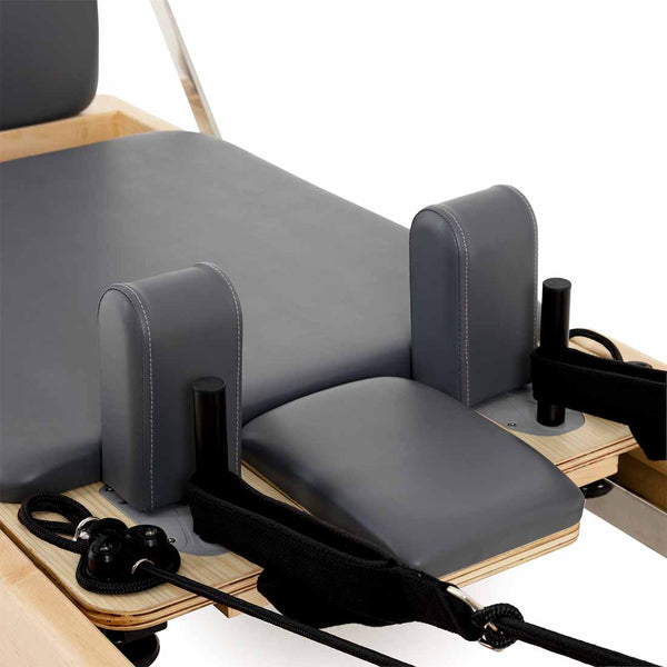 Close-up of the SMAI Pilates - Classical Maple Reformer, featuring padded gray cushions, black straps, and a durable maple wood frame for supportive, effective Pilates workouts.