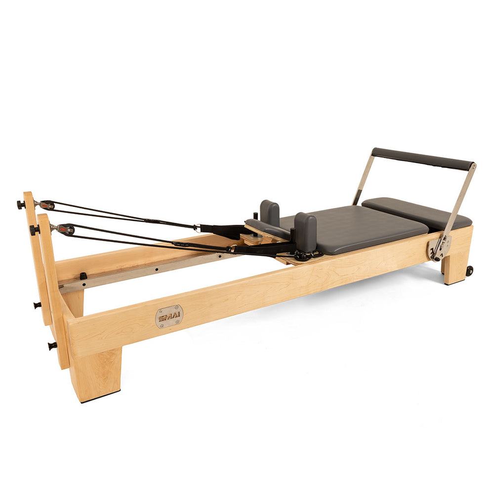 The SMAI Pilates - Classical Maple Reformer, featuring a padded sliding platform, adjustable foot bar, black shoulder rests, and resistance cords, is displayed on a white background.