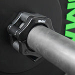 A close-up of a smooth Olympic barbell shows an Easy Lock 50mm Collar from SMAI. The black clamp securely holds the weight, with the collar ensuring stability before a partially visible plate with green lettering.