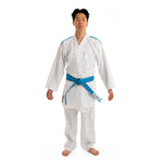 The individual is dressed in a WKF Reversible Karate Uniform - 6oz Premium Kumite Gi - Inazuma RX from SMAI, featuring a blue belt and blue accents. They stand barefoot against a plain white background.