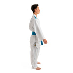 A person dressed in a SMAI WKF Reversible Karate Uniform - 6oz Premium Kumite Gi - Inazuma RX, featuring a white and blue design, stands in a side profile pose with a blue belt. The uniform showcases blue branding on the shoulder and side. This reversible jacket is ideal for competition Kumite Gi practice. The barefoot individual poses against a plain white background.
