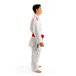 A person stands sideways wearing the SMAI WKF Reversible Karate Uniform - a 6oz Premium Kumite Gi, displayed with a red belt against a plain white background. The gi showcases distinctive red and black logos on the shoulders, embodying the Inazuma RX style. The individual is barefoot, ready for action.
